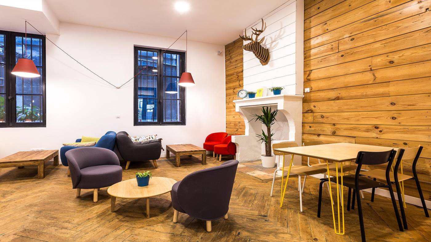 Espace de travail et de télétravail de l'Anticafé Bordeaux : cheminée, grandes tables et fauteuils